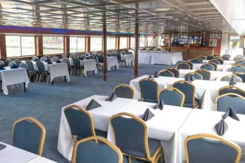 Interior of a dining area with tables, chairs, and blue carpet on a boat or ship.