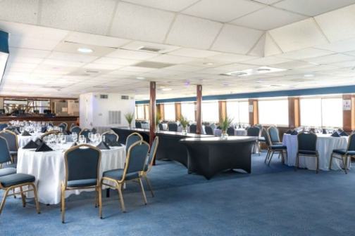 Spacious banquet hall with round tables, blue chairs, white tablecloths, and large windows.